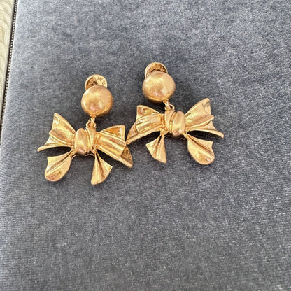 Gold-tone vintage metal bow stud earrings with round top accents and hanging bow drops.