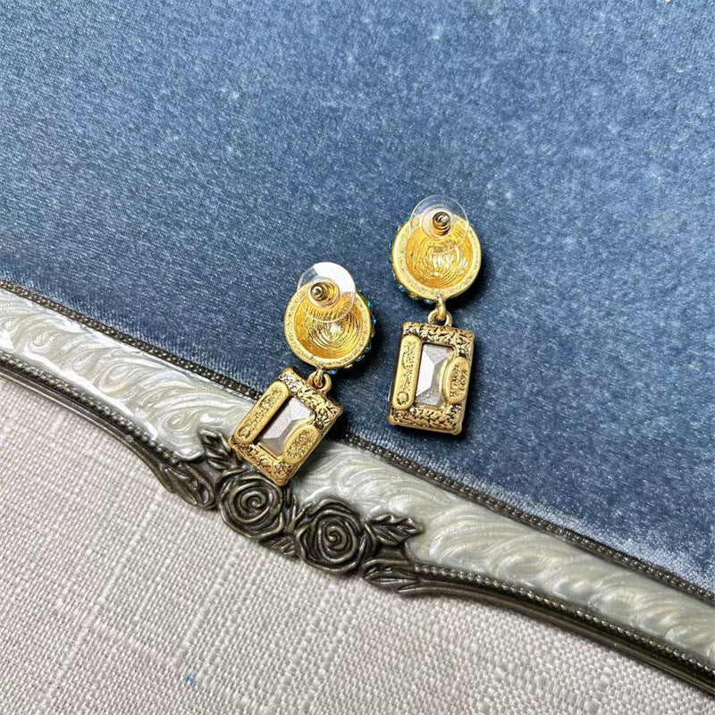 Gold-tone stud earrings with white square-cut drop stones and round jeweled caps