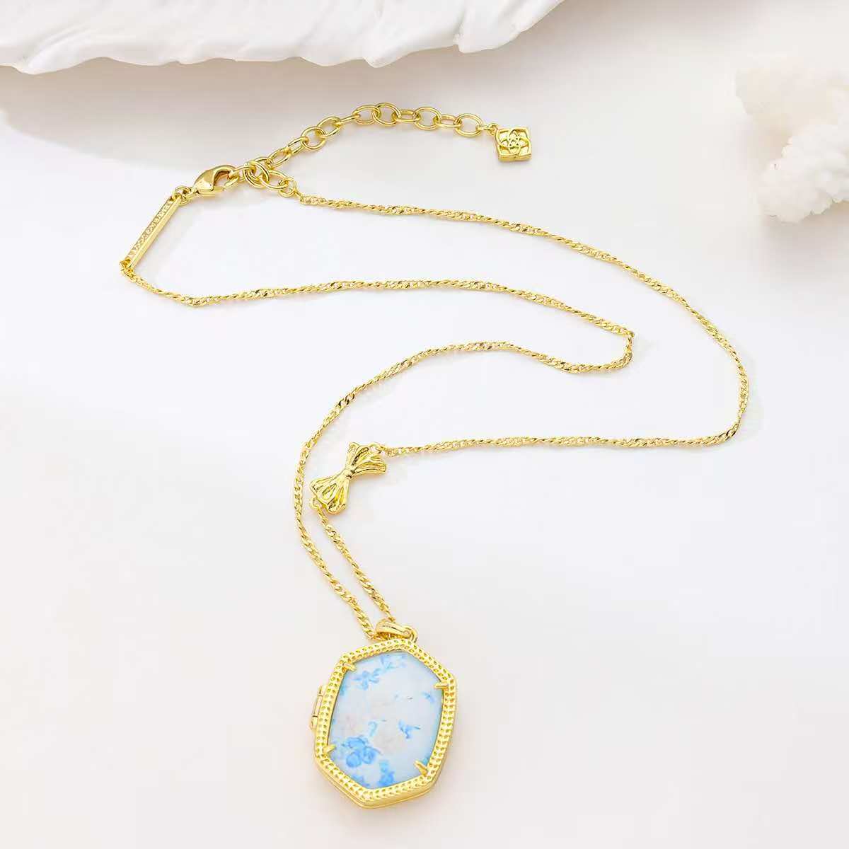 Gold-plated pendant necklace laid out with blue floral octagon pendant on chain