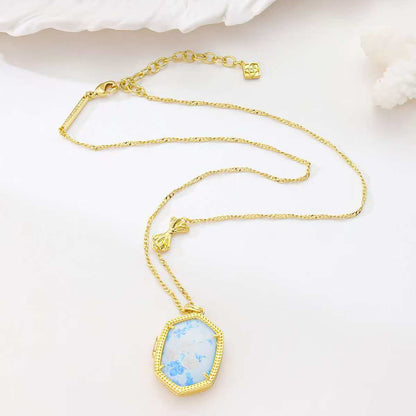 Gold-plated pendant necklace laid out with blue floral octagon pendant on chain