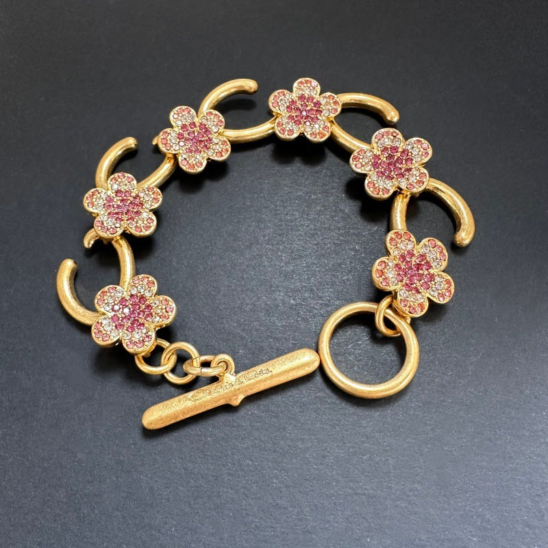 Gold-tone bracelet with pink flower charms, pave stones, and bar toggle clasp