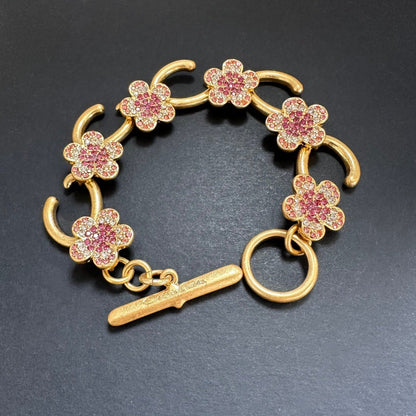 Gold-tone bracelet with pink flower charms, pave stones, and bar toggle clasp