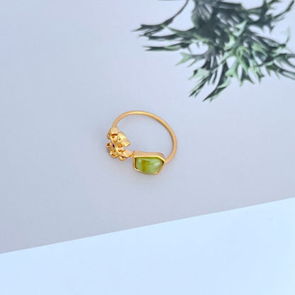 Gold-tone matte logo ring with green acrylic stone and ornate logo setting