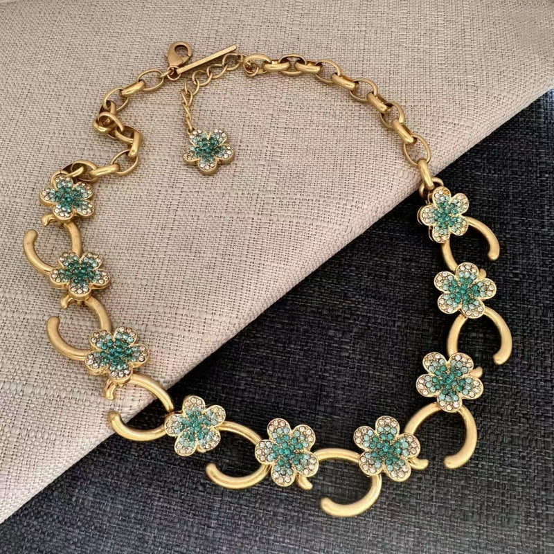 Gold-plated floral pendant necklace with teal rhinestone clover charms and curved links