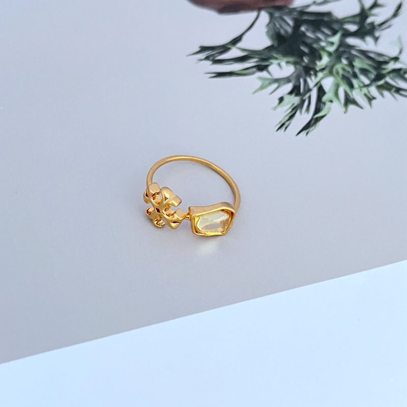 Gold-tone matte logo ring with transparent acrylic stone and ornate setting