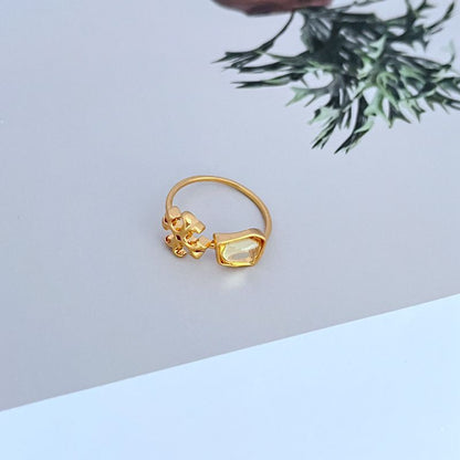 Gold-tone matte logo ring with transparent acrylic stone and ornate setting