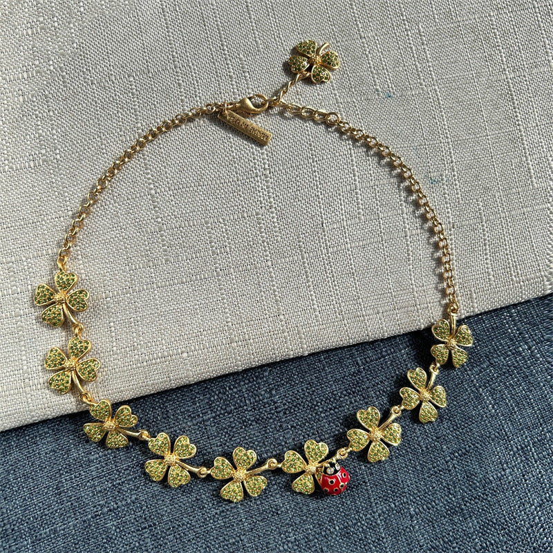 Gold-tone crystal clover necklace with dangling ladybug charm and heart-shaped links