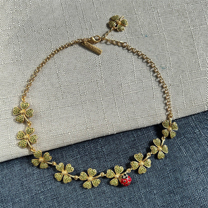 Gold-tone crystal clover necklace with dangling ladybug charm and heart-shaped links