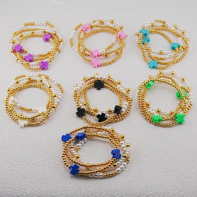 Assorted cross-charm pearl and gold beaded stackable bracelets in multiple colors