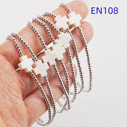 Close-up: silver-tone beaded bracelets with white cross charms stacked on hand