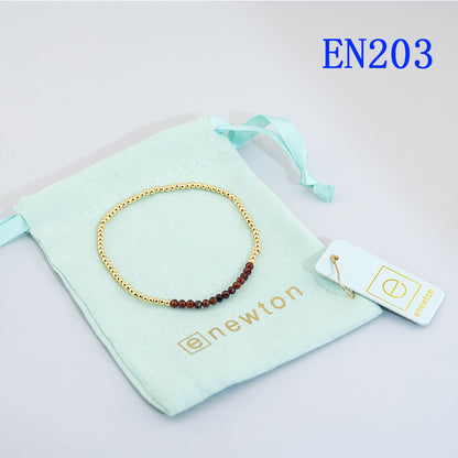 Elastic beaded bracelet with gold round beads and a dark red bead accent row.