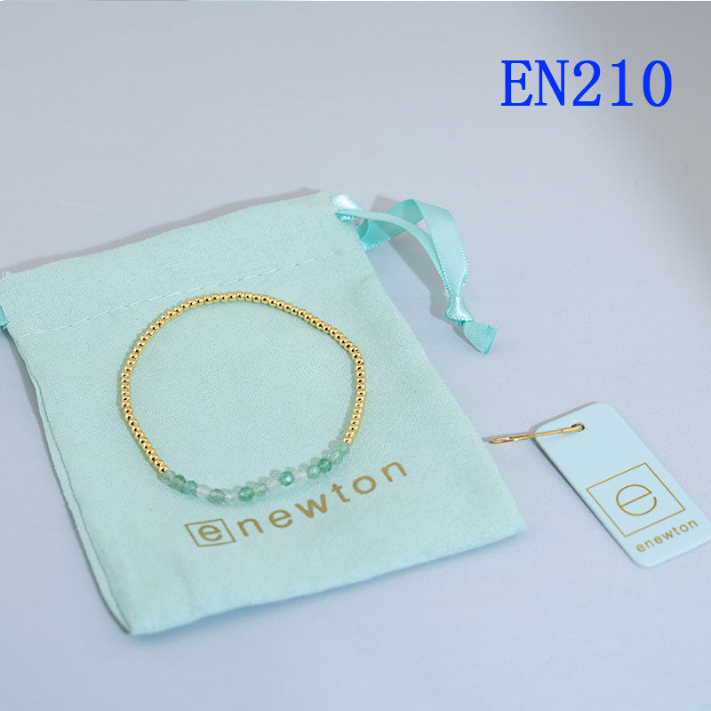 Elastic beaded bracelet with gold round beads and light blue bead accent row.