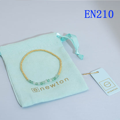Elastic beaded bracelet with gold round beads and light blue bead accent row.