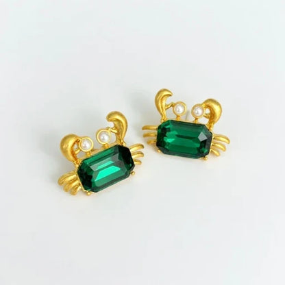 Crab-shaped crystal stud earrings with gold-tone settings, pearls, and a deep green gem
